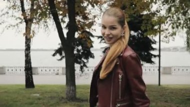 Sonbahar geliyor. Mutlu kadın bordo deri ceketli yürüyerek şehir sokak, slowmotion.