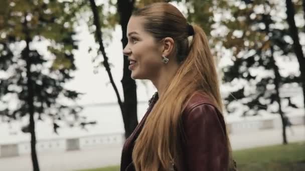 Наближається осінь. Щаслива жінка в бордовій шкіряній куртці ходить по міській вулиці, сповільнення . — стокове відео