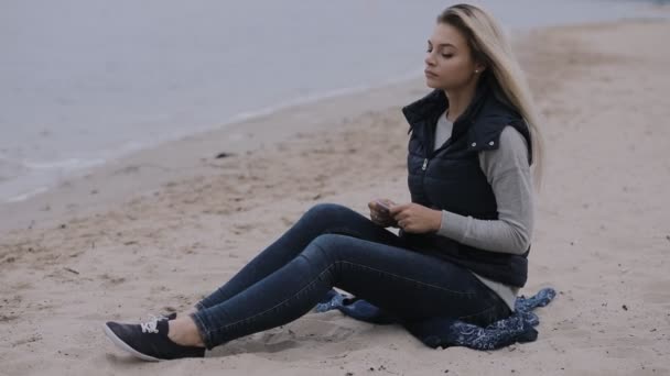 Día de otoño nublado frío. Mujer deprimida sentada en la playa del río, ella llora carta . — Vídeo de stock