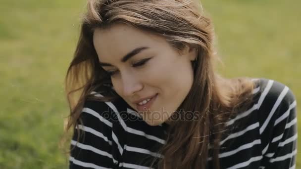 Gelukkige vrouw zitten op gras, close-up portret van schattig gezicht in slowmotion, ze knipoog — Stockvideo