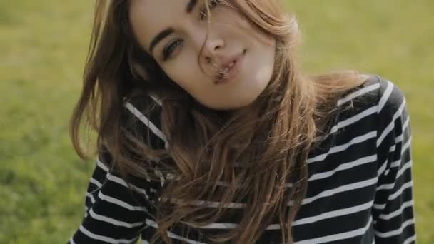 Щаслива жінка сидить на траві, крупним планом портрет милого обличчя в сповільненому темпі — стокове відео