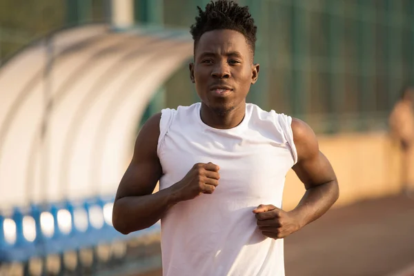 African male sportsman in a cap running on stadium track, he trains endurance — Stock Photo, Image