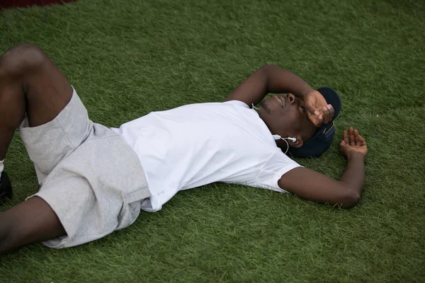 Fáradt afroamerikai férfi sportoló feküdt a füvön, kemény edzés után — Stock Fotó