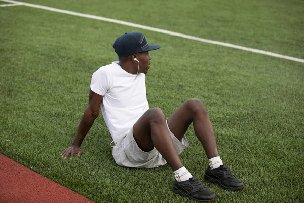 Afro-amerikai férfi sportoló ül a stadion fű, és hallgatni a zenét a fülhallgató — Stock Fotó