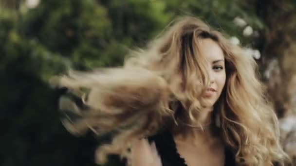 Красива жінка з завитими волоссям і сережками позує в міському зеленому парку, сповільнення — стокове відео