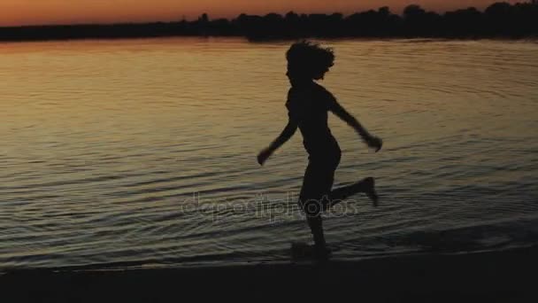 Silhouette de femme heureuse court autour de la rivière au coucher du soleil au ralenti — Video