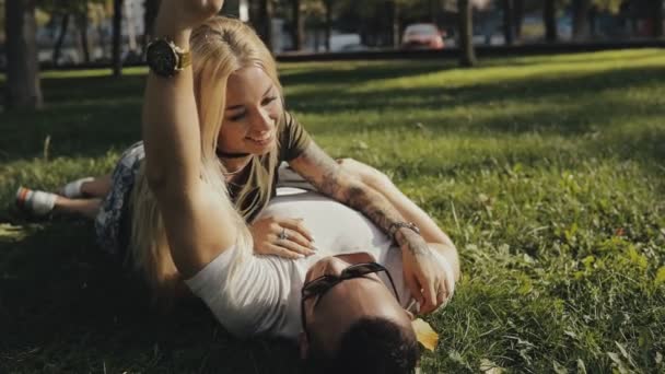 Feliz joven pareja acostada en la hierba en el parque y divertirse, slow motion — Vídeo de stock