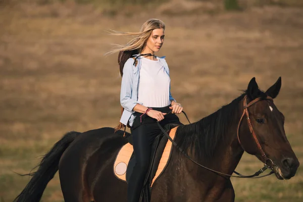 Schöne junge Cowgirl reitet ihr Pferd in Feld — Stockfoto