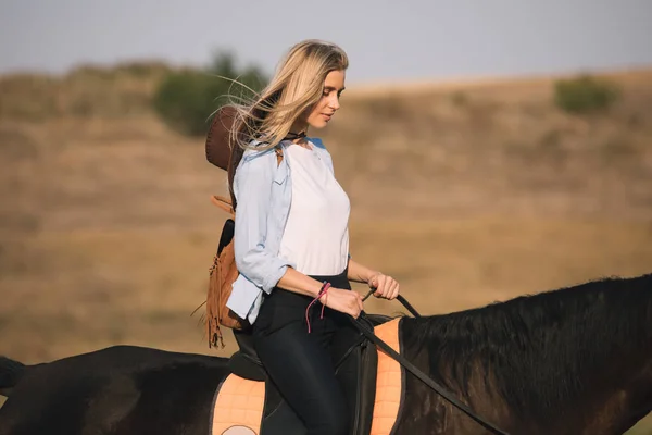 Schöne junge Cowgirl reitet ihr Pferd in Feld — Stockfoto