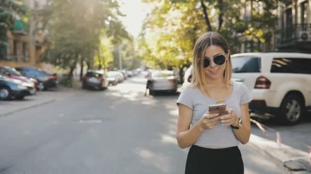 Женщина всегда связана. Она использует смартфон, гуляя по городской улице . — стоковое видео