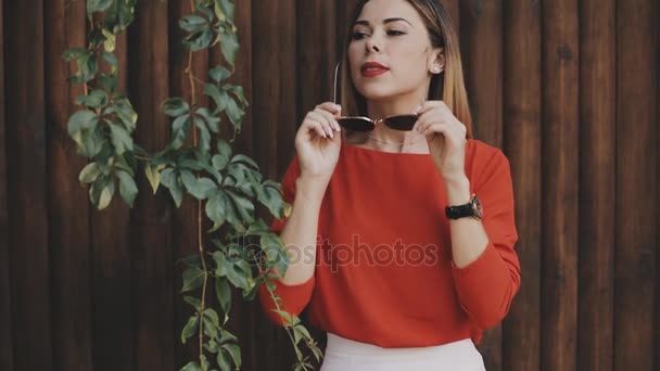 Jovem bela mulher retrato em óculos de sol perto de parede de madeira olhar tempo no relógio — Vídeo de Stock