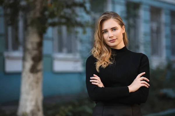 Porträtt av ung kvinna student mot blå universitet byggnaden bakgrund, armarna korsade — Stockfoto