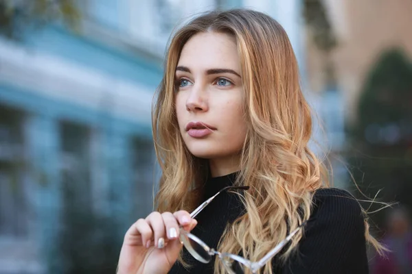 Bijziendheid, portret van een jonge vrouw student holding brillen voor goed zicht, blauwe gebouw achtergrond — Stockfoto