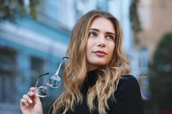 Krátkozrakost, portrét mladé ženy studenta drží brýle pro dobrý zrak, modrá budova pozadí — Stock fotografie