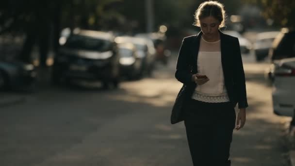 Jovem estudante mulher confiante em terno clássico ir na estrada olhando para baixo para telefone inteligente na cidade — Vídeo de Stock