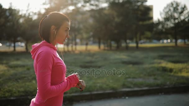 Hübsche Sportlerin in rosa Sportbekleidung beim Joggen im Freien, gesundes Lifestylekonzept. Zeitlupe. sie misst die Zeit auf der Stoppuhr. — Stockvideo