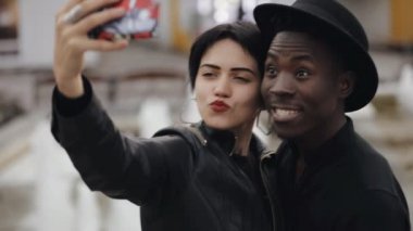 Beyaz kadın ve zenci çift Slowmotion selfie smartphone geçici video. Yanağını öptü. Onlar gülümseyen, birlikte gülüyor.