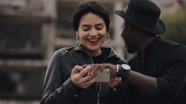 Slowmotion beyaz kadın ve zenci çift smartphone cep telefonu ile video aşağı bakıyor. Onlar birlikte gülüyor, video çok saçma.