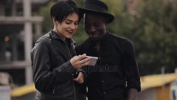 Lento movimento da mulher branca e do casal homem negro olhando para baixo para vídeo no smartphone. Eles rindo juntos, vídeo é muito ridículo . — Vídeo de Stock