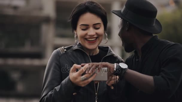 Slowmotion λευκή γυναίκα και μαύρο άντρα ζευγάρι κοιτάζοντας προς τα κάτω βίντεο σε smartphone. Αυτοί που γελά μαζί, το βίντεο είναι πολύ γελοίο. — Αρχείο Βίντεο