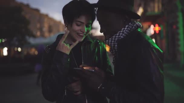 Rallentamento della donna bianca e nero coppia uomo guardando verso il basso per lo schermo sullo smartphone durante la notte. Loro sorridono, ridono . — Video Stock