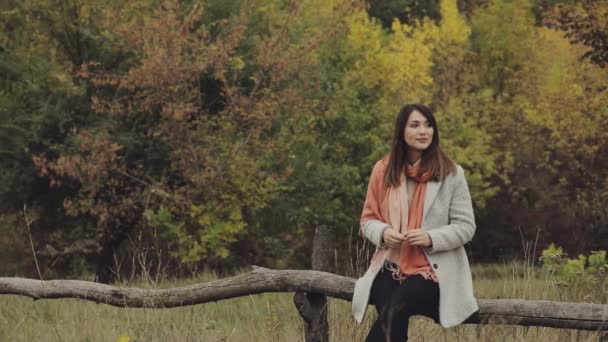 Gelukkig jonge vrouw genieten van de herfst zittend op houten hek op platteland natuur, langzame motie — Stockvideo