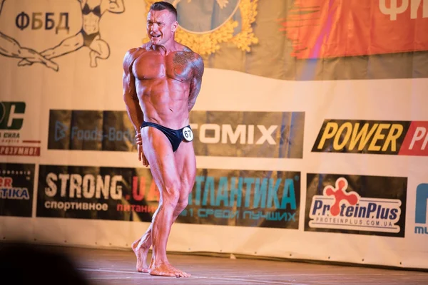 UKRAINE, DNEPR - OCTOBER 08, 2017: Bodybuilding konkurrence show. Åbnet mesterskab. Stærk musculars atlet mand poserer på en scene . - Stock-foto