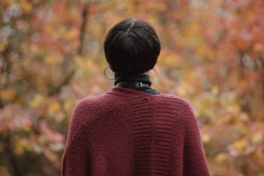 Arka plan üzerinde marsala renk hırka sonbahar orman, bulanık sarı yapraklar içinde tanınmayan sıradışı kadın arkadan görünüş