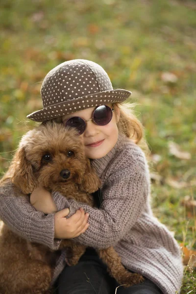 Çim sarılma köpek sonbahar gününde birlikte oturan şapkalı mutlu küçük kız — Stok fotoğraf