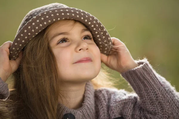 Fashion closeup portrait of little girl wearing hat sitting on a grass in autumn clothes — Stock Photo, Image