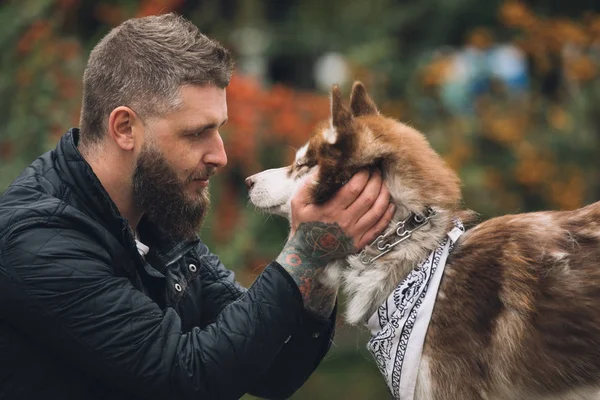 Retrato del hombre con un perro husky se mira en el parque en el día de otoño —  Fotos de Stock