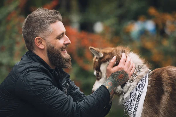 Retrato del hombre jugando con su perro husky en el parque en el día de otoño — Foto de Stock