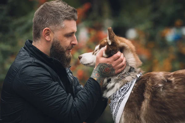 Retrato del hombre con un perro husky se mira en el parque en el día de otoño — Foto de Stock