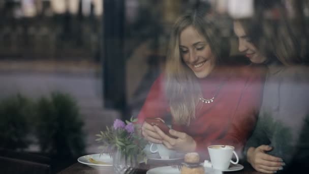Друзья-женщины пользуются смартфоном в кафе, смотрят в окно — стоковое видео