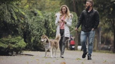 Erkek ve kadın sonbahar günü, yavaş hareket ile birlikte parkta husky köpek yürüyüş