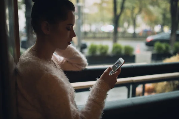 Adult girl using smartphone in cafe sit at window — Stock Photo, Image