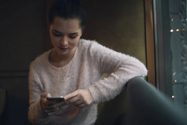Aikuinen tyttö käyttää älypuhelinta kahvilassa istua ikkunassa — kuvapankkivalokuva