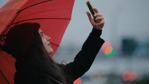 Gelukkige vrouw onder de paraplu van de rode mobiele foto maken — Stockvideo