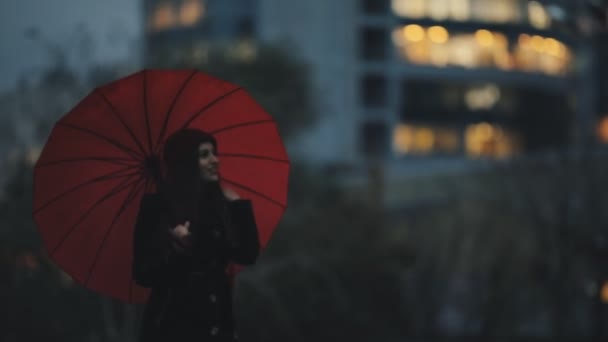 Ευτυχισμένη γυναίκα κάτω από την κόκκινη ομπρέλα, περπατώντας στο κέντρο της πόλης — Αρχείο Βίντεο