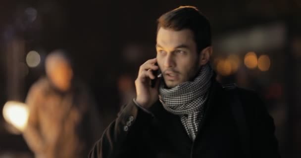 Бизнесмен идет и разговаривает по мобильному смартфону в ночном городе — стоковое видео