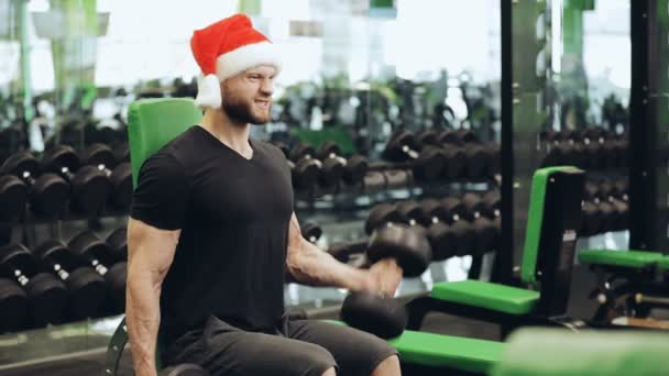 Siłownia, człowiek w Santa hat pompowania biceps — Wideo stockowe
