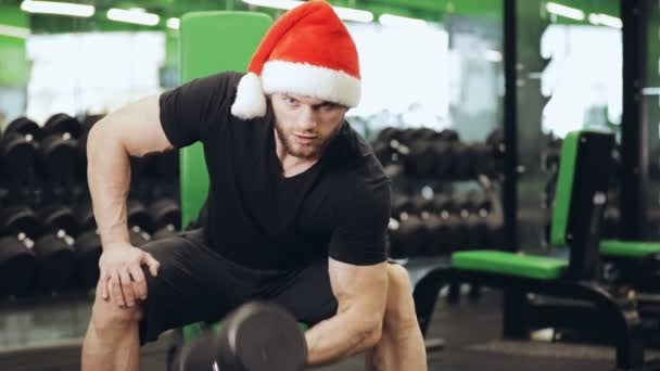 Fitness studio, mann mit weihnachtsmann-hut, der bizeps pumpt — Stockvideo