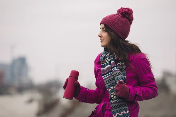妇女在明亮的冬天夹克拿着热水瓶与茶在城市背景 — 图库照片