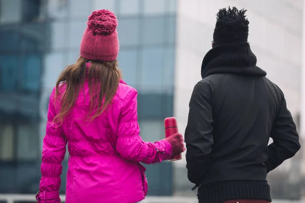 Dos amigos multirraciales juntos en la ciudad de invierno, vista trasera, ella sosteniendo termos — Foto de Stock