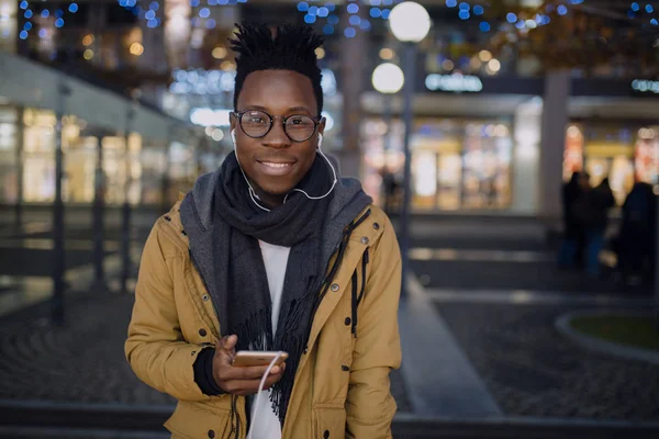 Африканських людина слухати музику в смартфон стоячи в темну ніч city, він посміхається камери — стокове фото