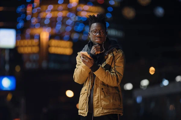 Африканських людина слухати музику в смартфон стояти під ночі холодні зимові міста — стокове фото