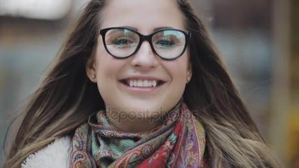 Portret van een jonge vrouw met donkerbruine haren en brillen glimlachend in een stad — Stockvideo