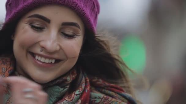 Joven mujer feliz en sombrero violeta mirando hacia arriba y sonriendo a la cámara en una ciudad — Vídeos de Stock