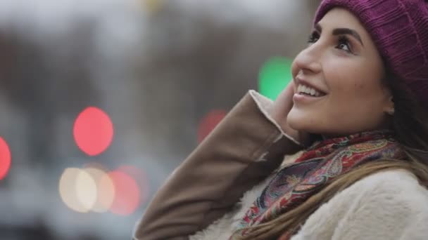 Joven mujer feliz en sombrero violeta mirando hacia arriba y sonriendo a la cámara en una ciudad — Vídeos de Stock