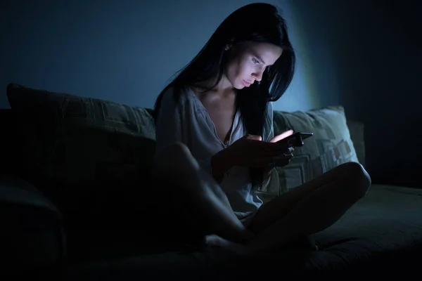 Уставшая женщина с синим экраном смартфона ночью в темной комнате — стоковое фото